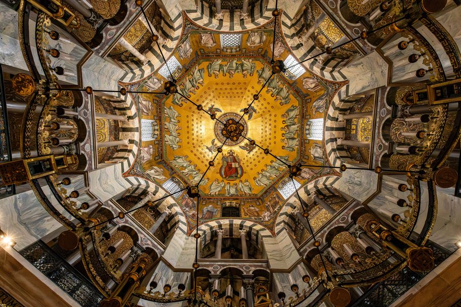 Looking up into the dome of the octagon of Aachen Cathedral, covered with gold mosaics and ringed by arches