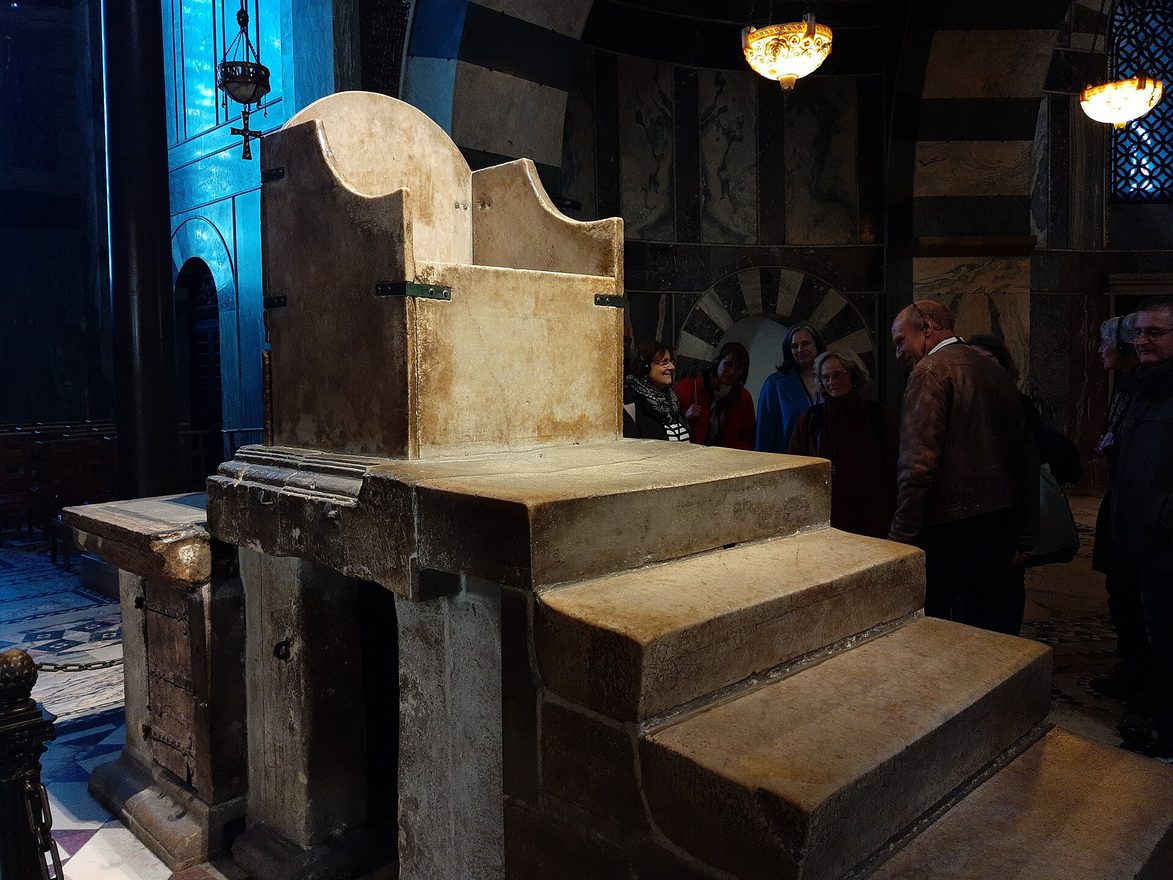 The plain marble throne of Charlemagne on its stepped platform in the upper gallery of Aachen Cathedral