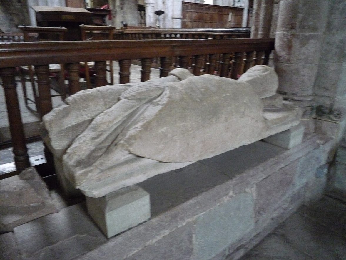 A worn medieval stone effigy of a knight lying on a low tomb chest in Dore Abbey