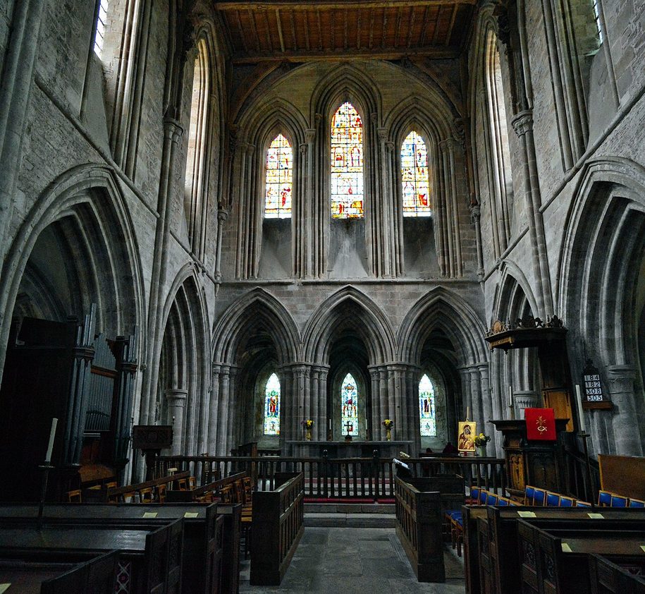 The presbytery of Dore Abbey, tall pale stone arches and lancet windows filled with stained glass above the altar