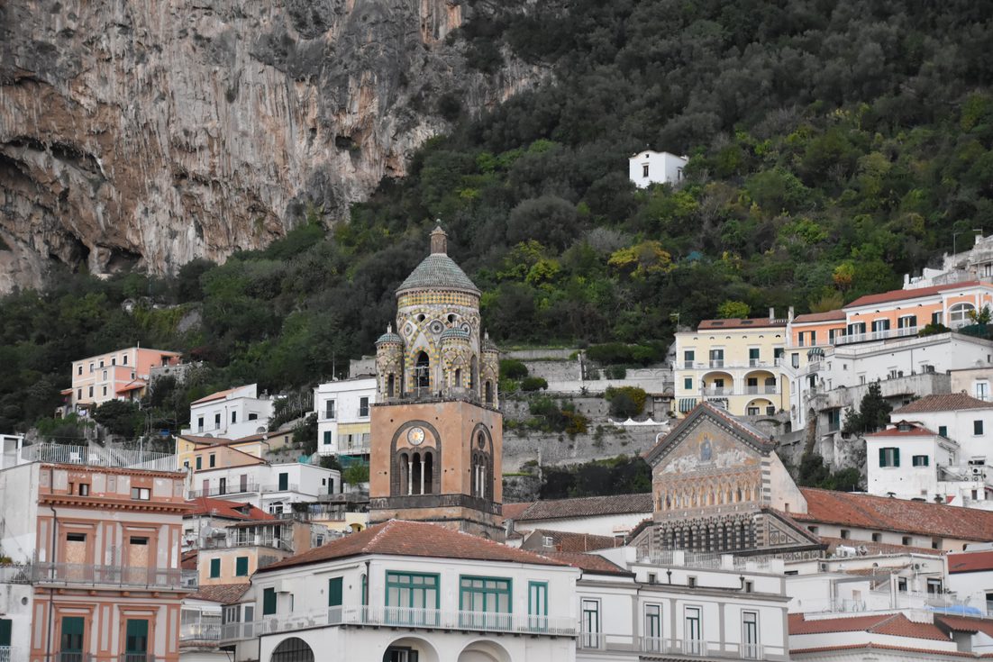 The bell tower and dome of Amalfi Cathedral rising above the pastel houses of Amalfi at the foot of steep wooded cliffs