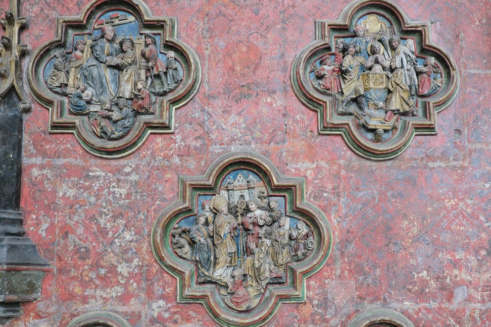 Painted stone reliefs in quatrefoil frames on the choir screen of Amiens Cathedral, against a red background