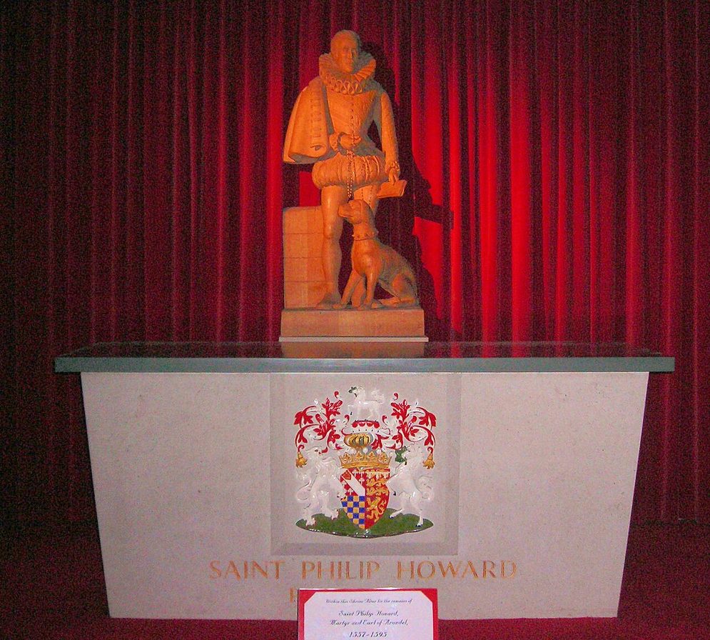 The shrine of St Philip Howard in Arundel Cathedral, a pale stone tomb chest carved with his coat of arms, with a wooden statue of the saint and his dog above