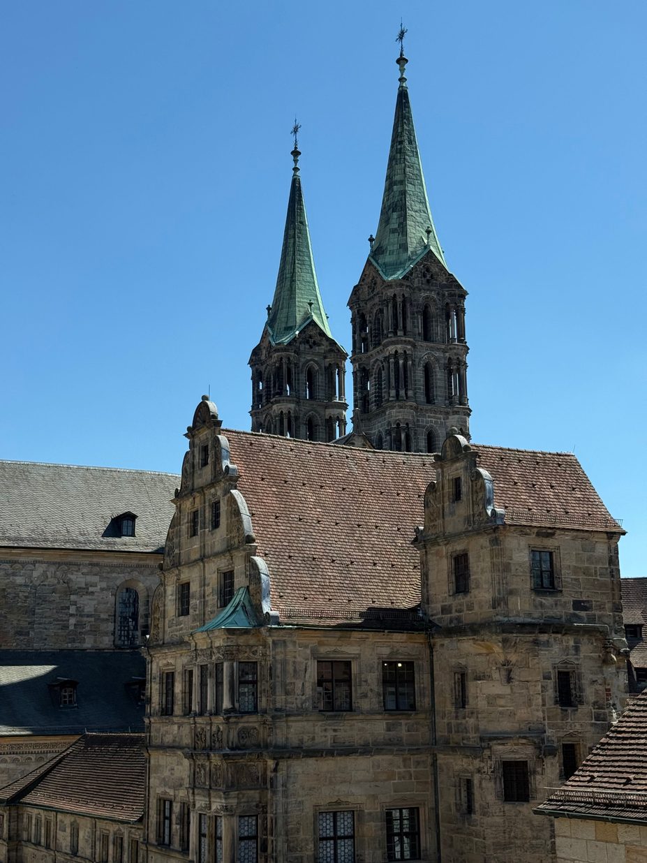 The two west towers of Bamberg Cathedral with green pointed spires, rising behind the gabled Renaissance range of the Alte Hofhaltung