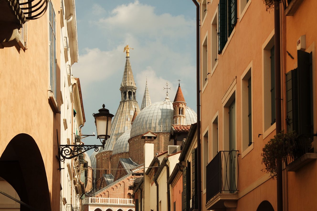 The domes and spires of the Basilica of St Anthony rising at the end of a street of arcaded houses in Padua