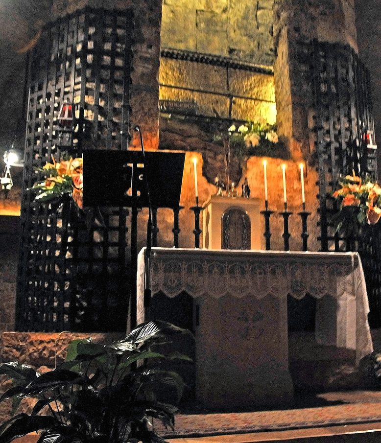 The stone tomb of St Francis behind a grille in the crypt of the basilica in Assisi, lit by lamps