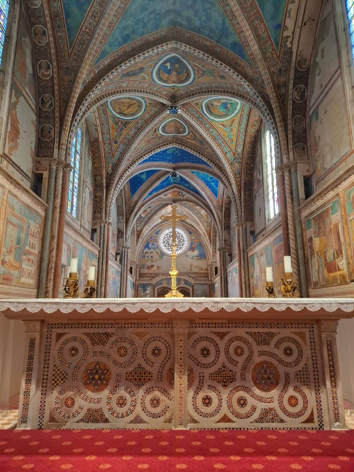 The Gothic nave of the Upper Basilica in Assisi, with frescoed walls and blue vaults painted with stars