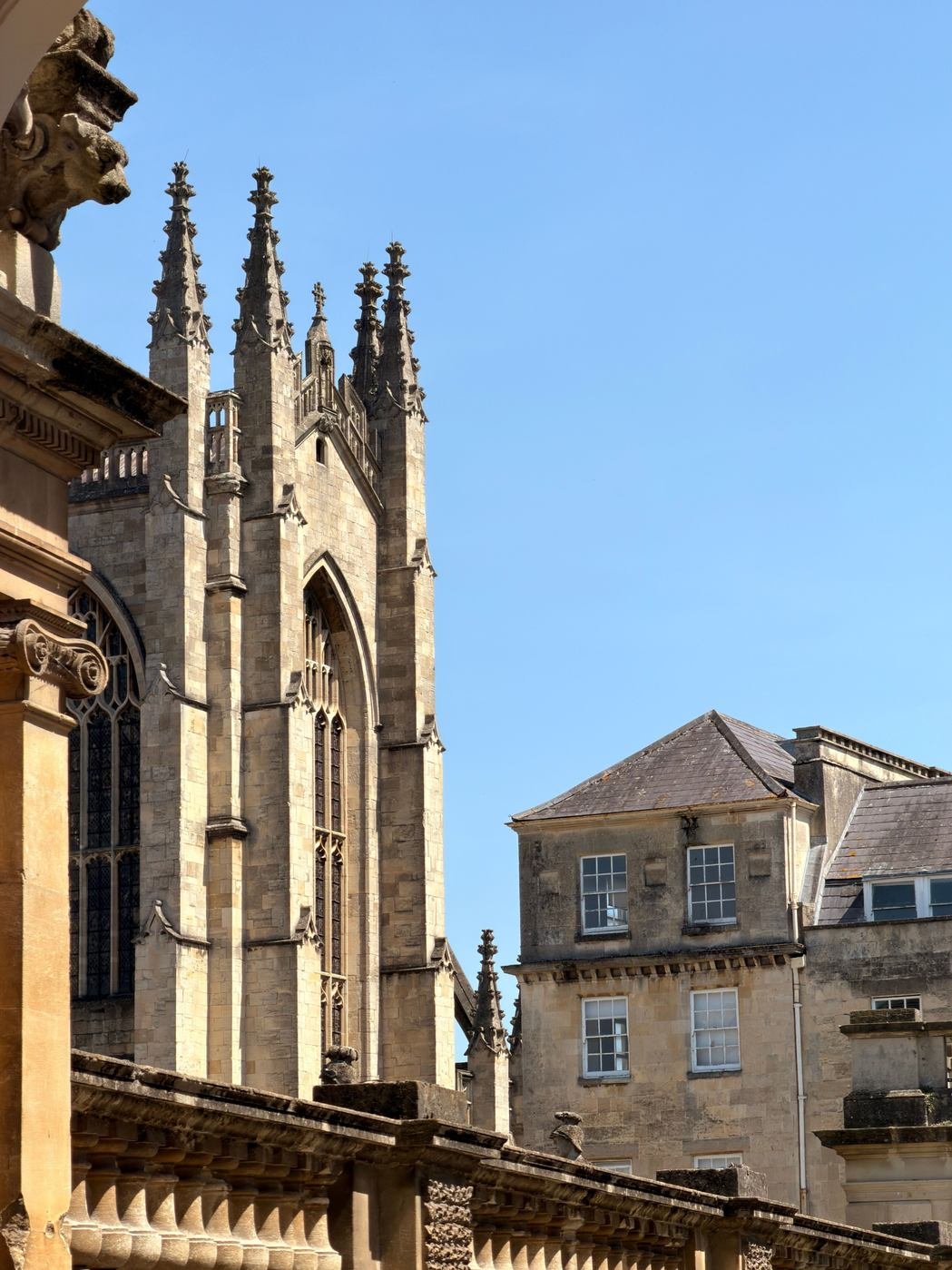 The pinnacles and buttresses of Bath Abbey against a blue sky