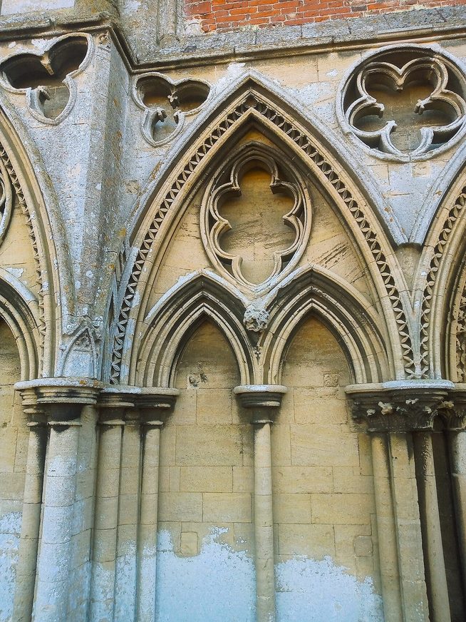 Detail of the carved stone arcading and tracery of the west front of Binham Priory, with pale blue sky through the openings