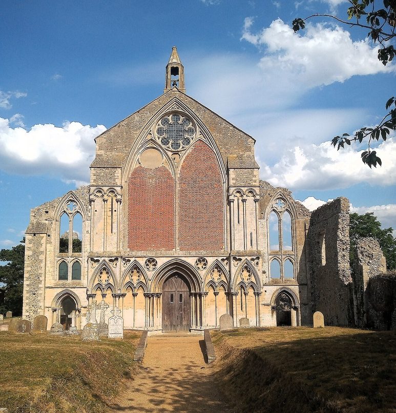 The west front of Binham Priory in Norfolk, a tall stone gable with a great bricked-up Gothic window above a row of arches