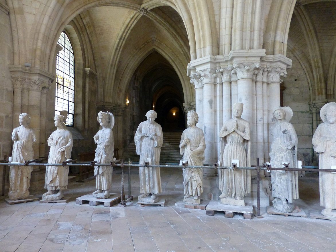 A row of white Gothic stone statues standing in the vaulted lower church of Bourges Cathedral