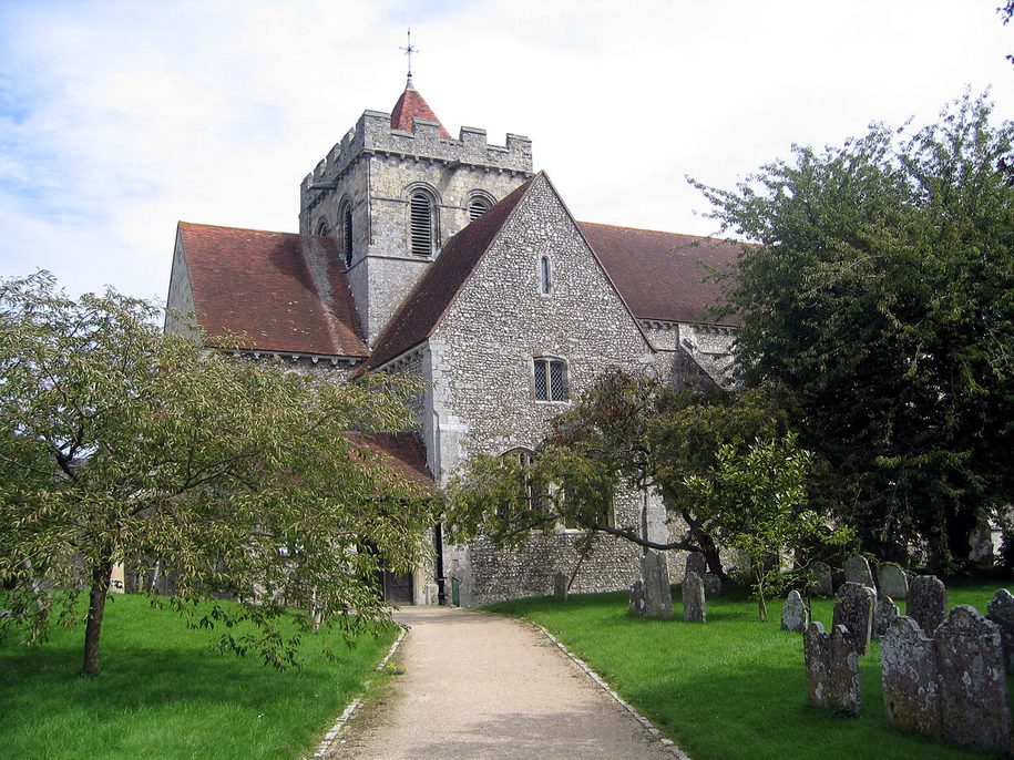Boxgrove Priory church in West Sussex, a flint and stone church with a low central tower, among trees and graves