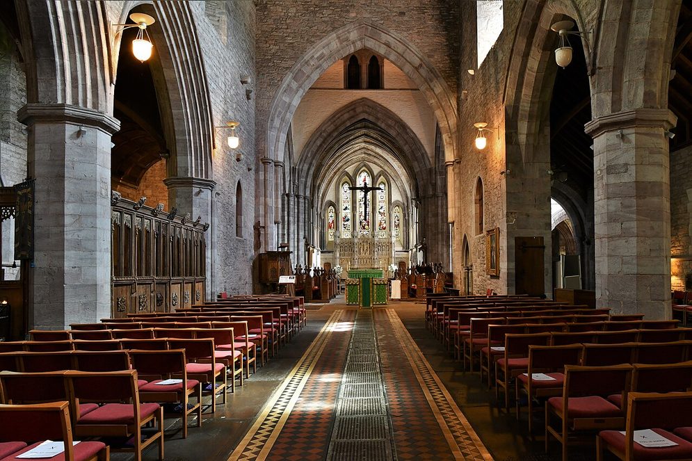 The nave of Brecon Cathedral looking east, with pointed arcades, rows of chairs and the chancel arch beyond