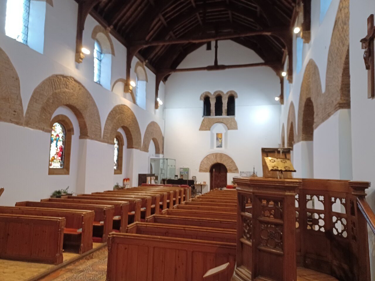 The tall white nave of Brixworth church looking west, with blocked round arches in the walls and a triple opening high in the west wall