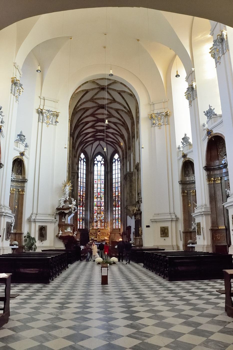 The white Baroque nave of Brno cathedral with a chequered floor leading to the Gothic choir