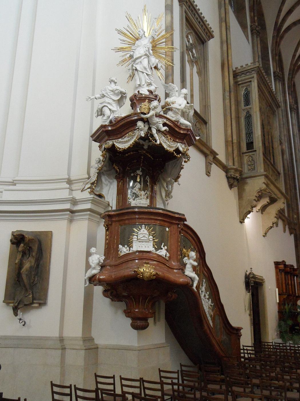 The white and gold Baroque pulpit of Brno cathedral topped by a statue
