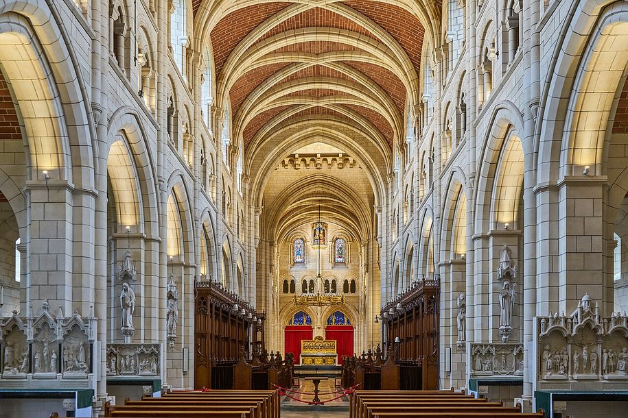 The long white stone nave of Buckfast Abbey with round arches and a ribbed stone vault, looking east to the altar