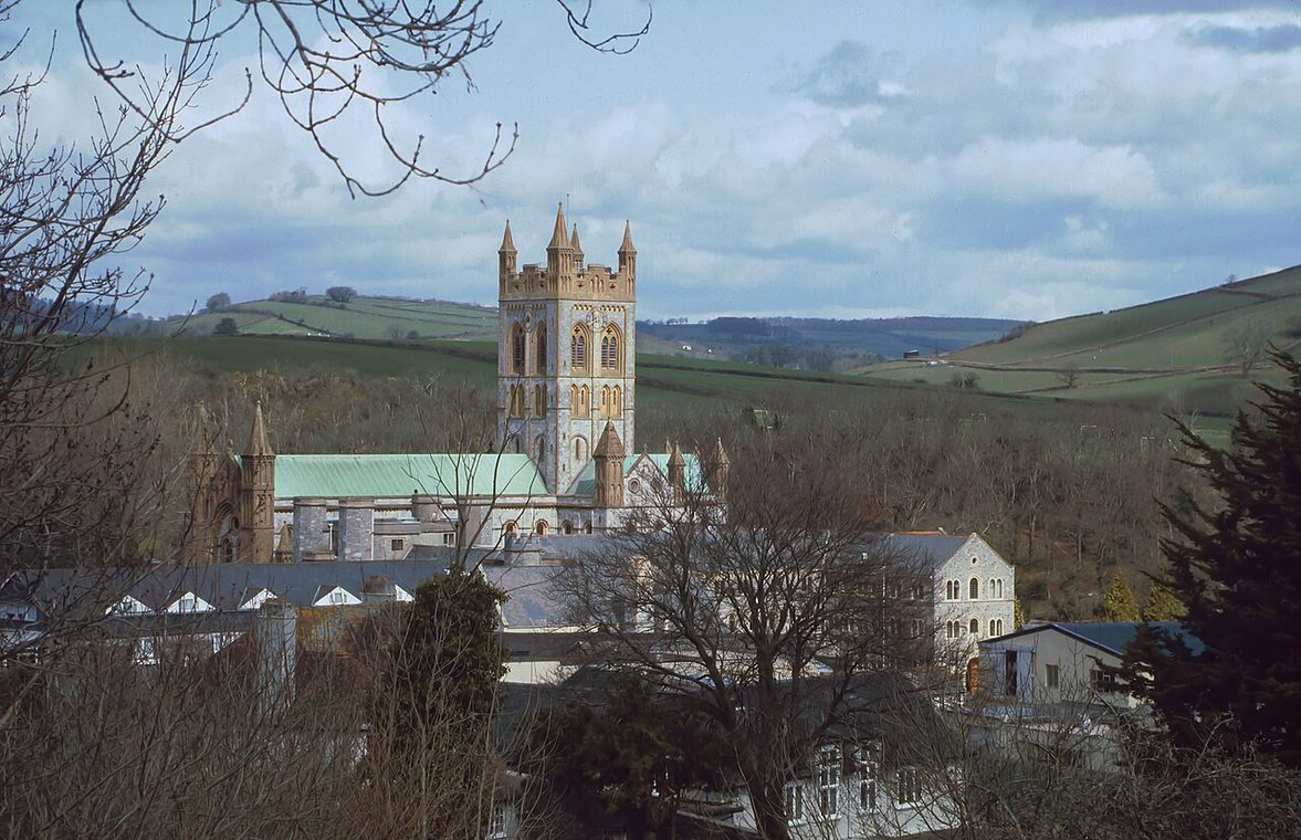 Buckfast Abbey seen across the Dart valley, its tower rising above the trees and roofs