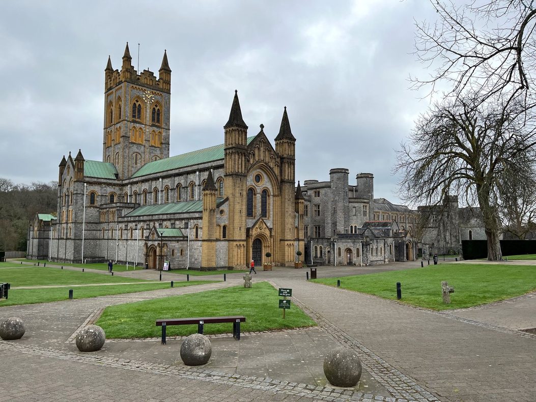 Buckfast Abbey church in Devon, a grey stone Romanesque-style church with a square central tower, seen across the lawns