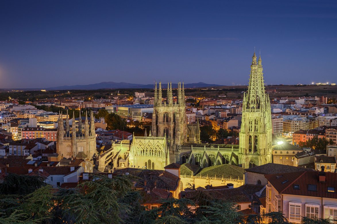 Burgos Cathedral lit up at dusk above the roofs of the city