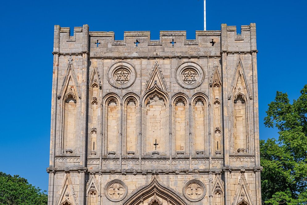 The fourteenth-century Abbey Gate of Bury St Edmunds, a tall decorated stone gatehouse with battlements, under a blue sky