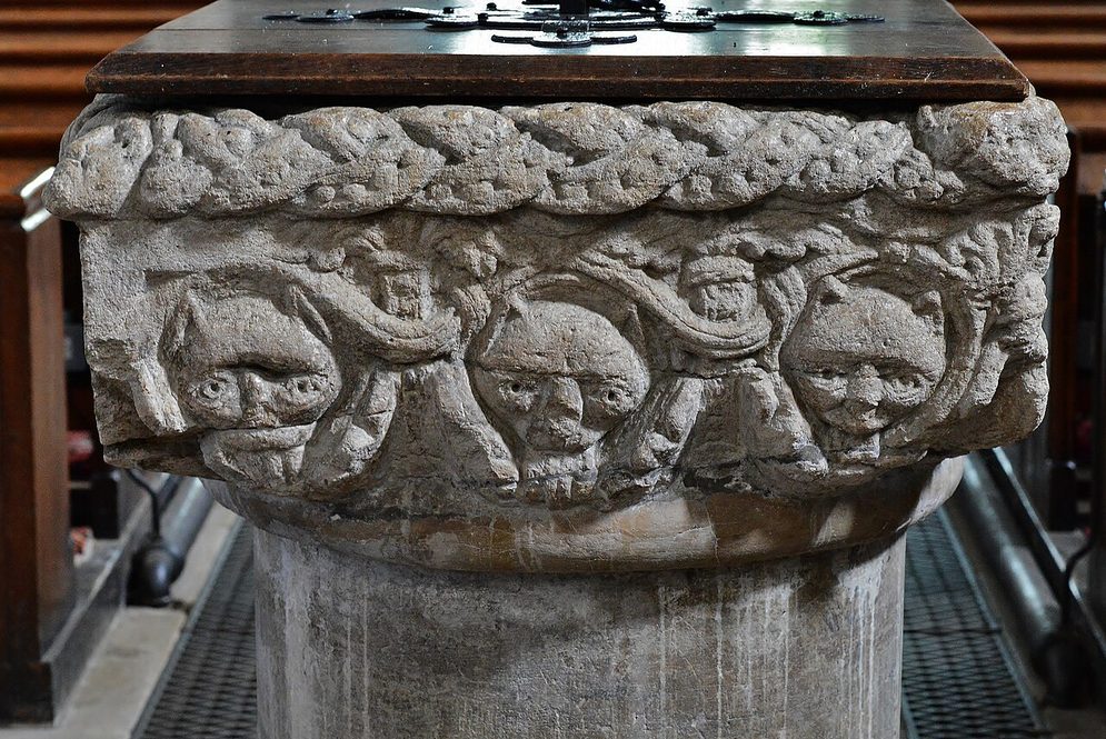 The square Norman font at Castle Rising, its bowl carved with a plait border and faces