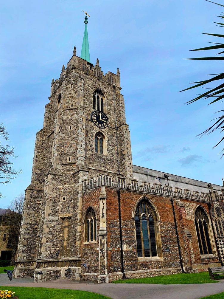 The flint tower of Chelmsford Cathedral with its clock and slender spire against a blue sky