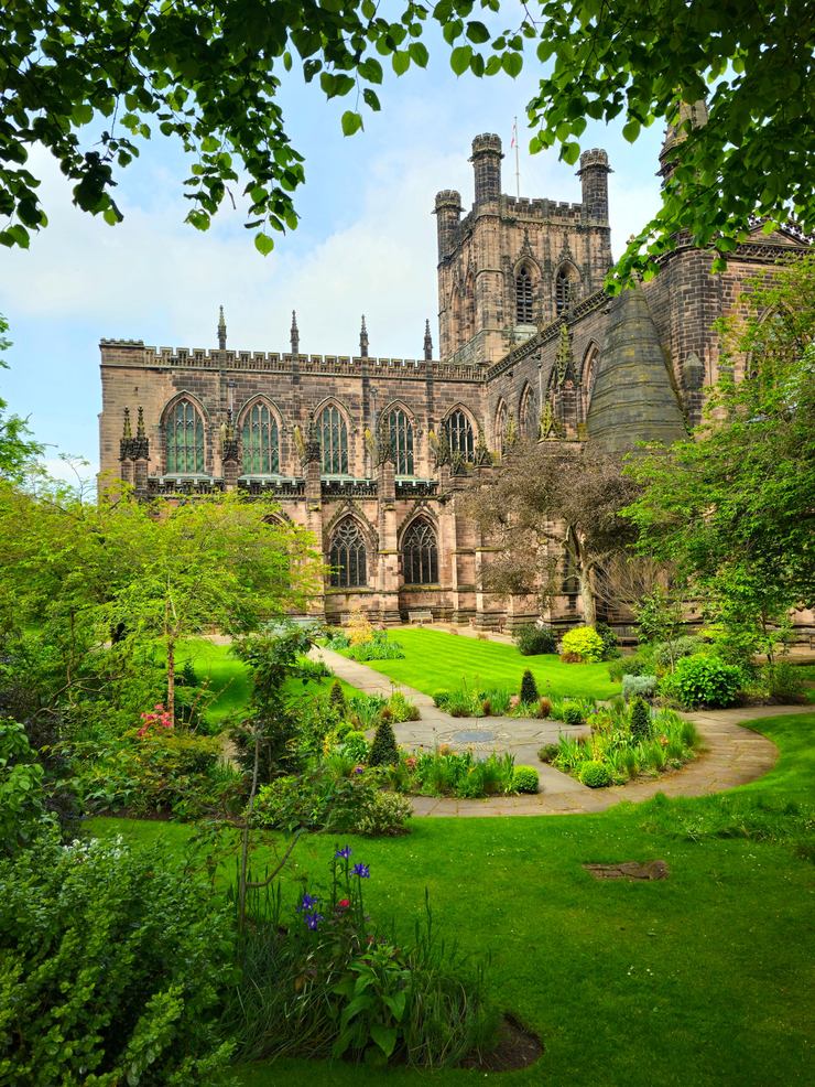 Chester Cathedral seen across a garden with green lawns and trees
