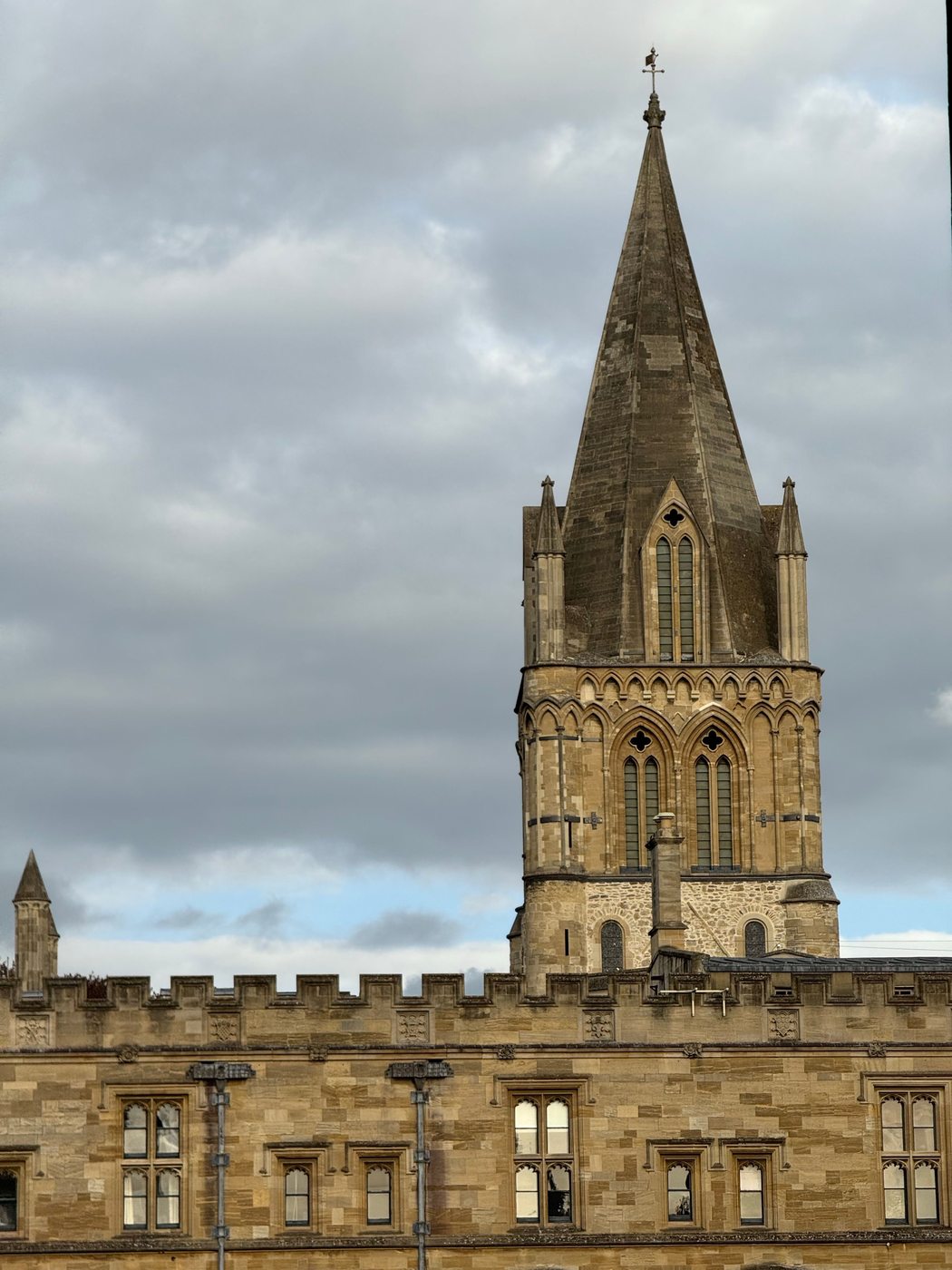 The thirteenth-century spire of Christ Church Cathedral above a battlemented college roof