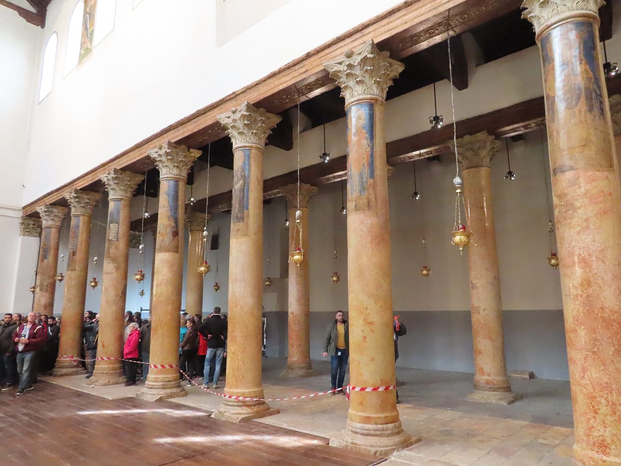 The long nave of the Church of the Nativity with rows of red limestone columns and hanging lamps
