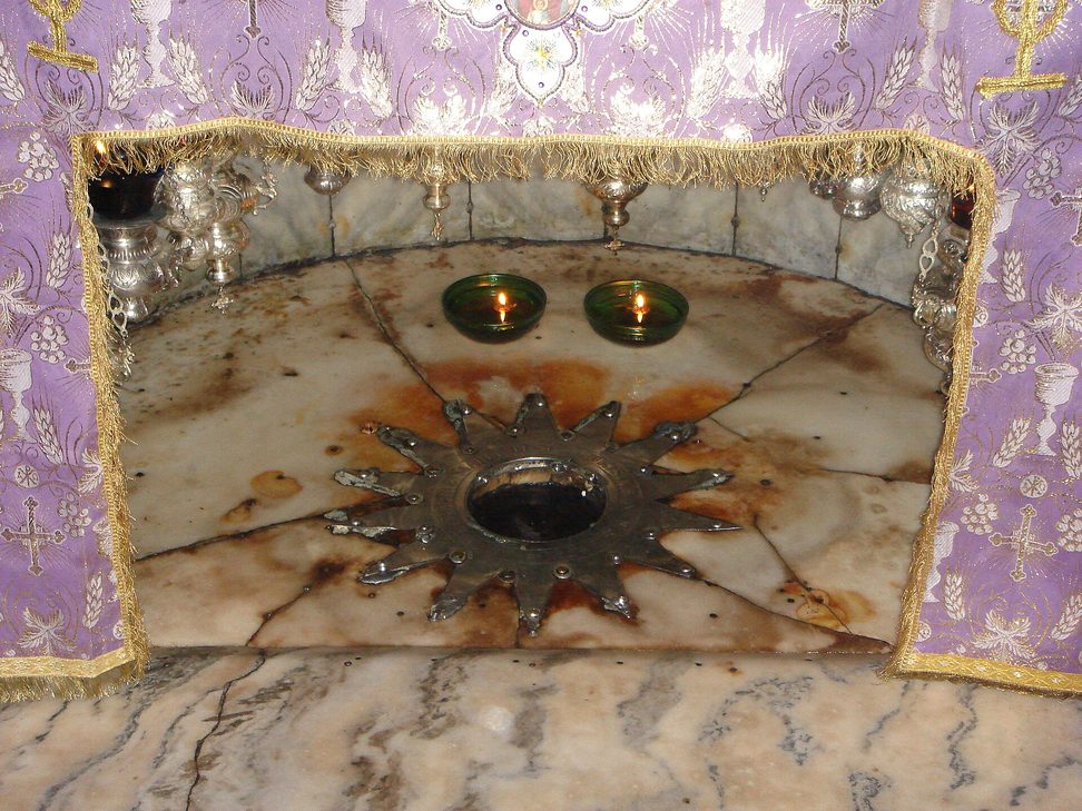 The silver star set in marble in the Grotto of the Nativity, surrounded by hanging lamps