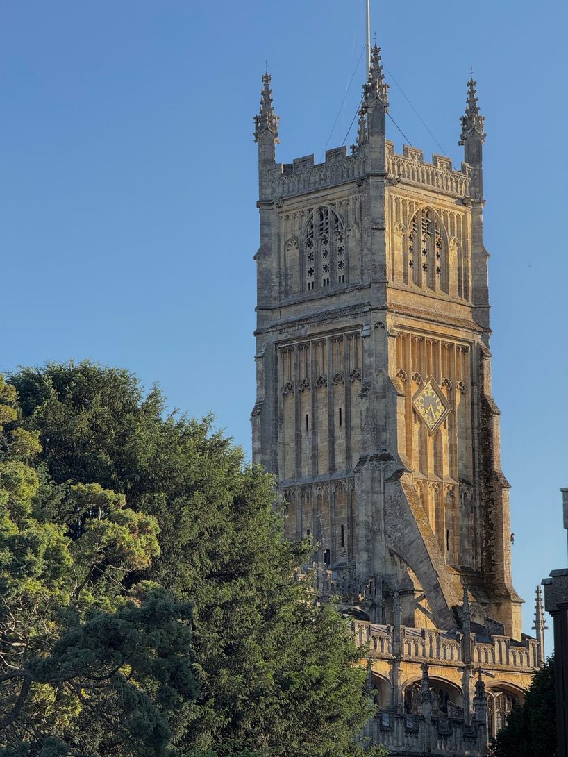 The tall Perpendicular tower of Cirencester parish church, with its pinnacles, against a blue sky