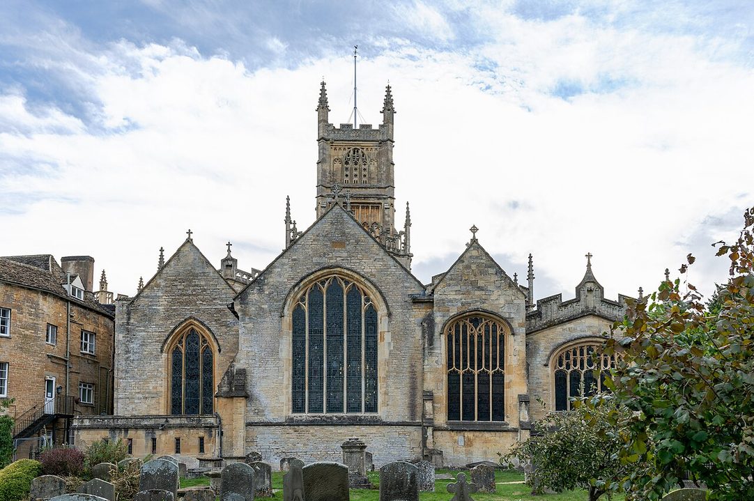 The church of St John Baptist in Cirencester seen from the Abbey Grounds, its tall pinnacled tower rising above the long Perpendicular nave