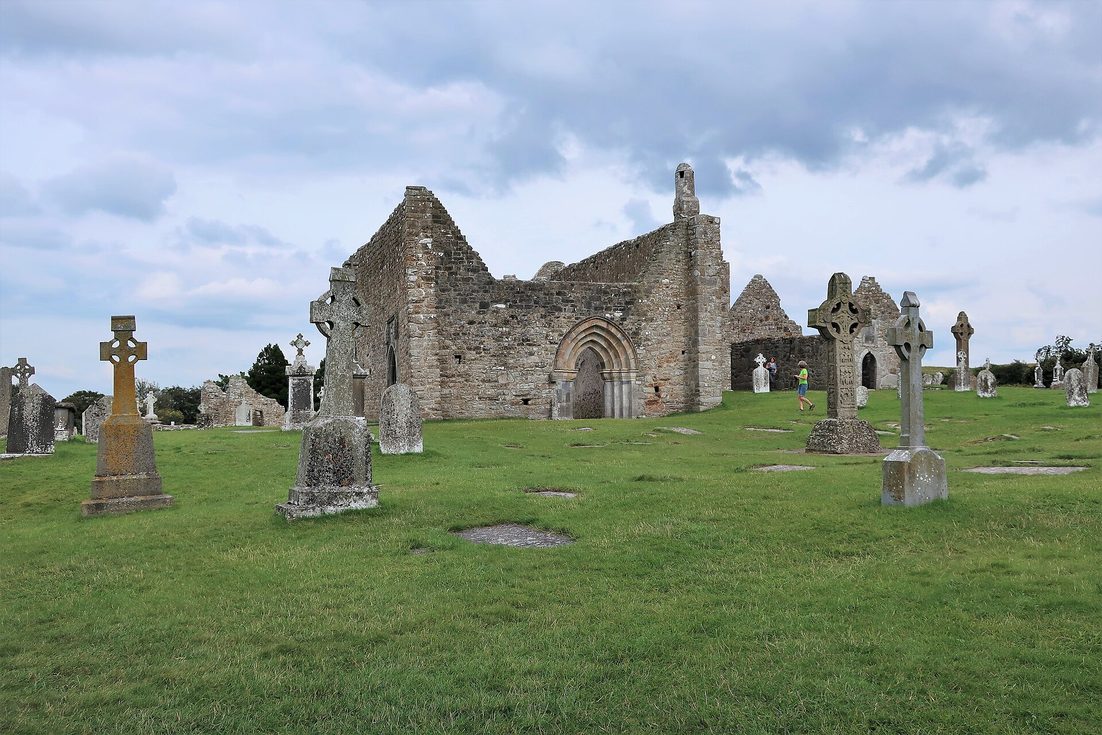 The roofless stone cathedral at Clonmacnoise with its tall west gable, among grave slabs and crosses