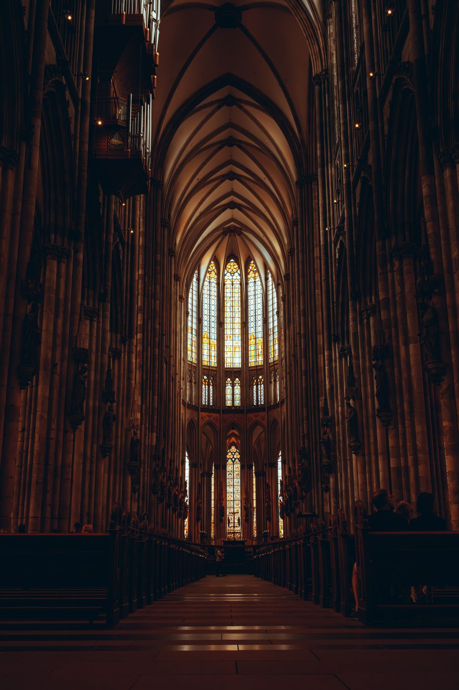 The long dark nave of Cologne Cathedral leading to the brightly lit stained glass of the choir