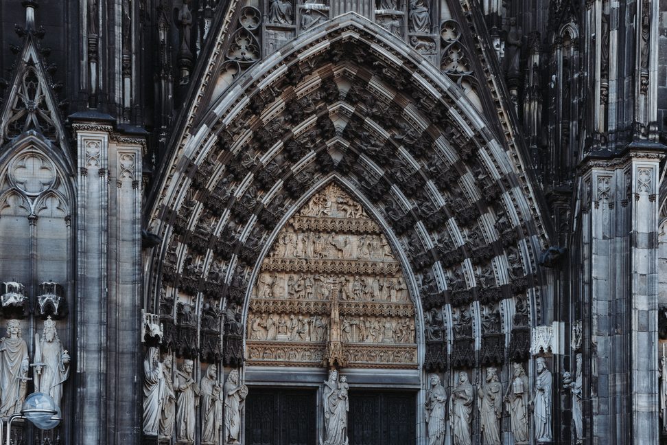 A deep Gothic portal of Cologne Cathedral, its arches lined with rows of carved figures
