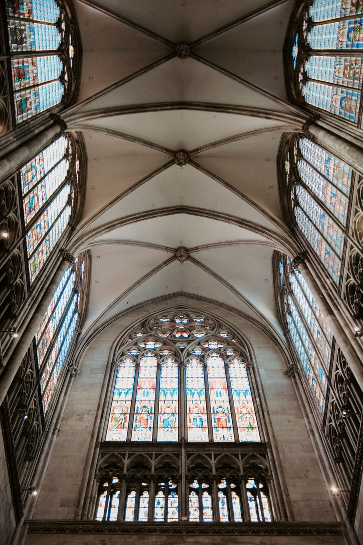 The ribbed vault and tall stained glass windows of a transept of Cologne Cathedral, seen from directly below