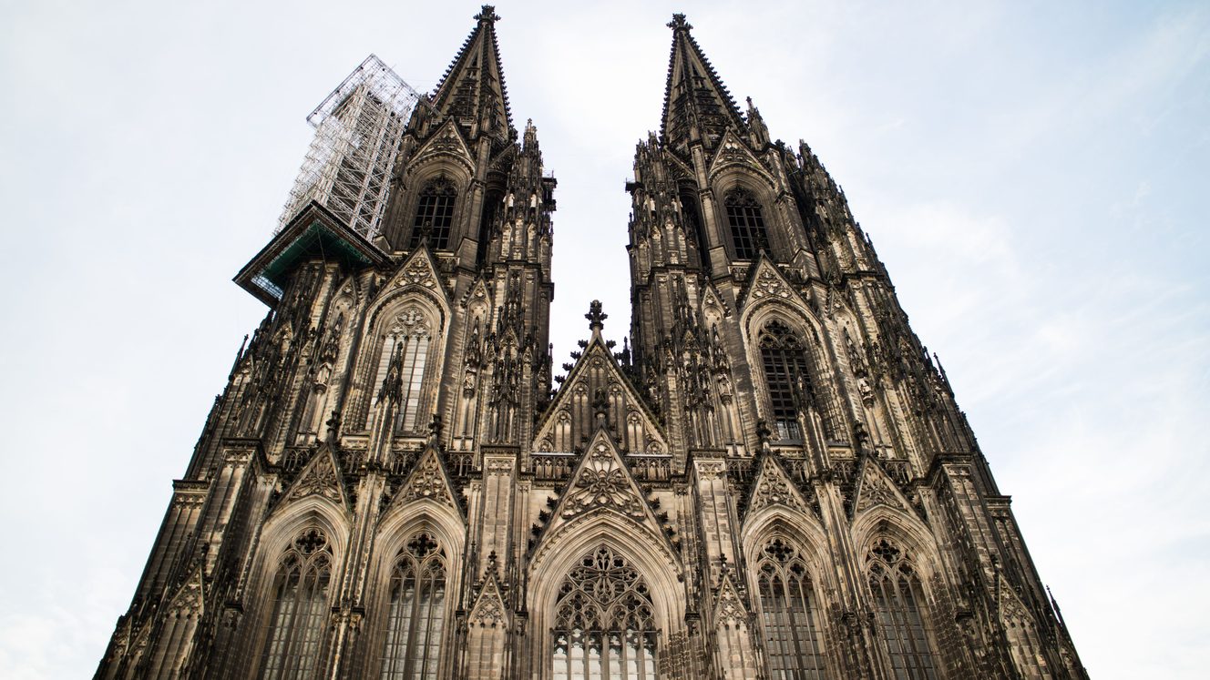 The twin Gothic spires and west front of Cologne Cathedral seen from below against a pale sky