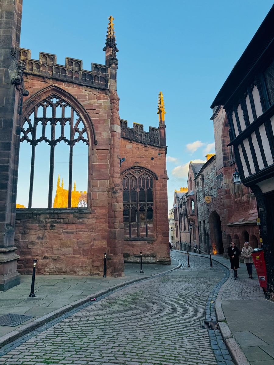 The ruined walls of old Coventry Cathedral seen from a cobbled street