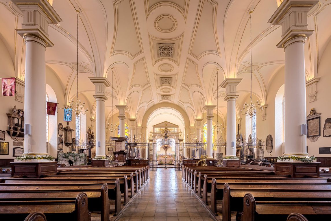 The light Georgian interior of Derby Cathedral, with white columns, a decorated plaster ceiling and the wrought-iron screen at the far end