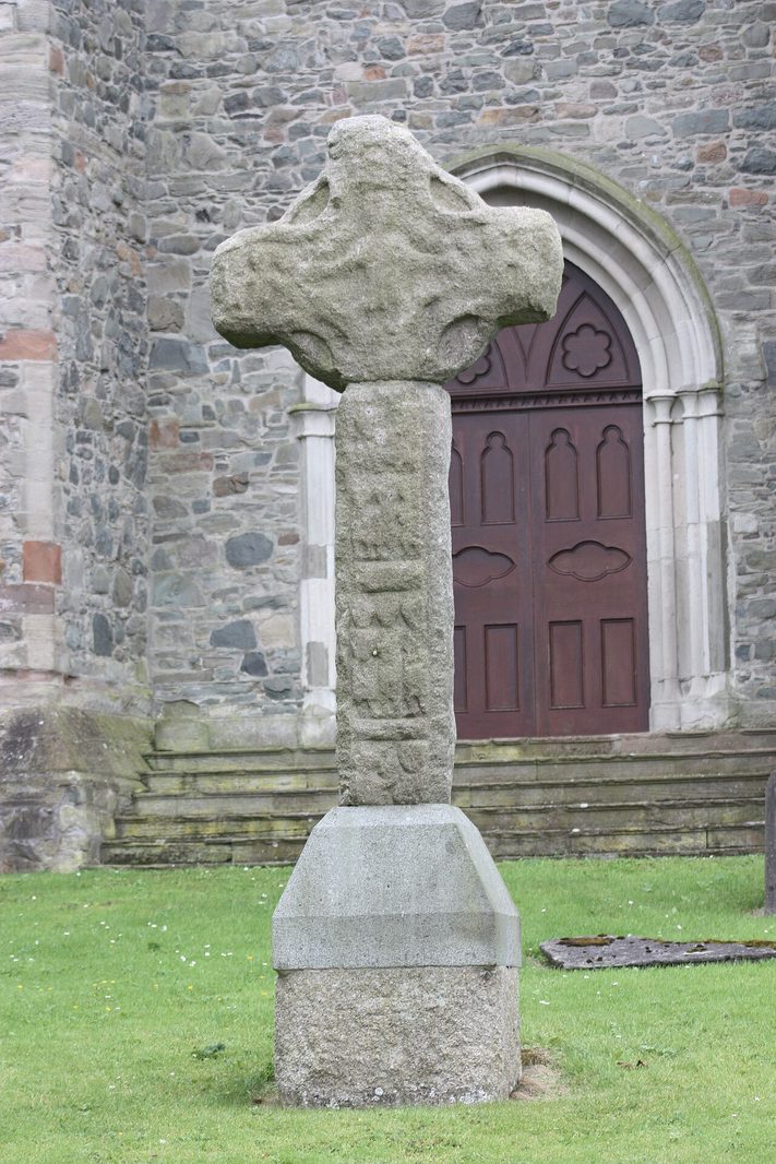 The stone high cross on the grass outside Down Cathedral, in front of a doorway