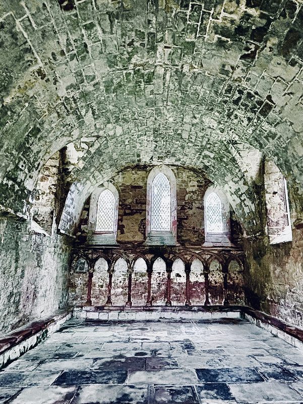 Inside the barrel-vaulted chapter house of Dryburgh Abbey, with a row of small arches along the east wall below three windows