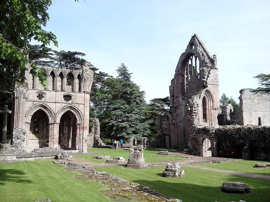 The ruined pink sandstone church of Dryburgh Abbey, its transept gables standing among cedars and lawns