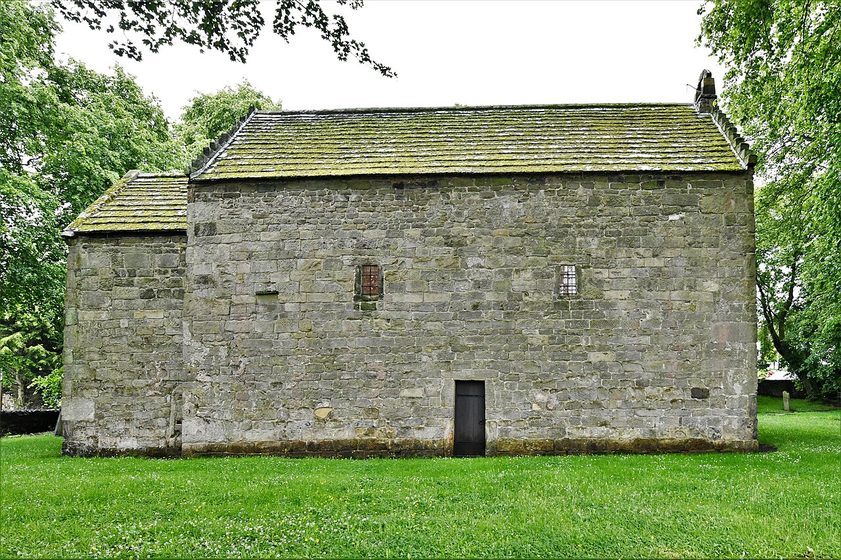 The north side of Escomb church, with large squared stones, tiny high windows and a stone-slate roof