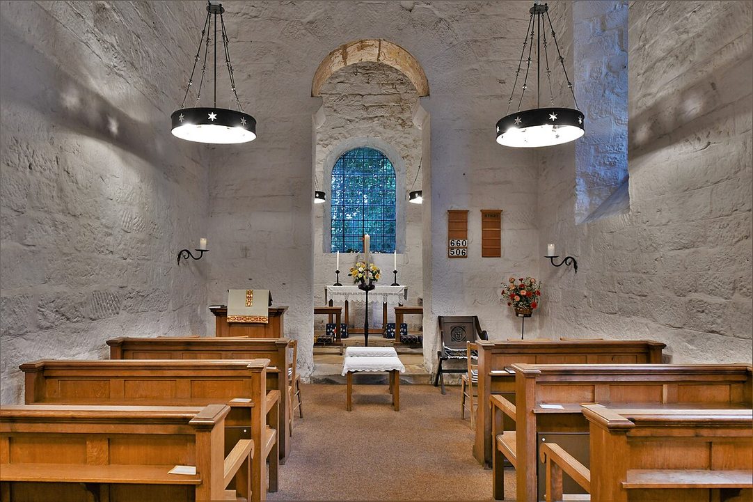The tall, narrow whitewashed nave of Escomb church looking east to a tall round chancel arch