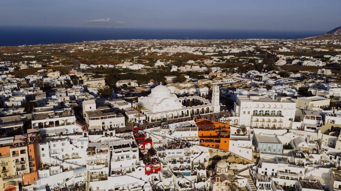 Aerial view of the white houses of Fira spilling down the cliff edge above the blue sea of the caldera