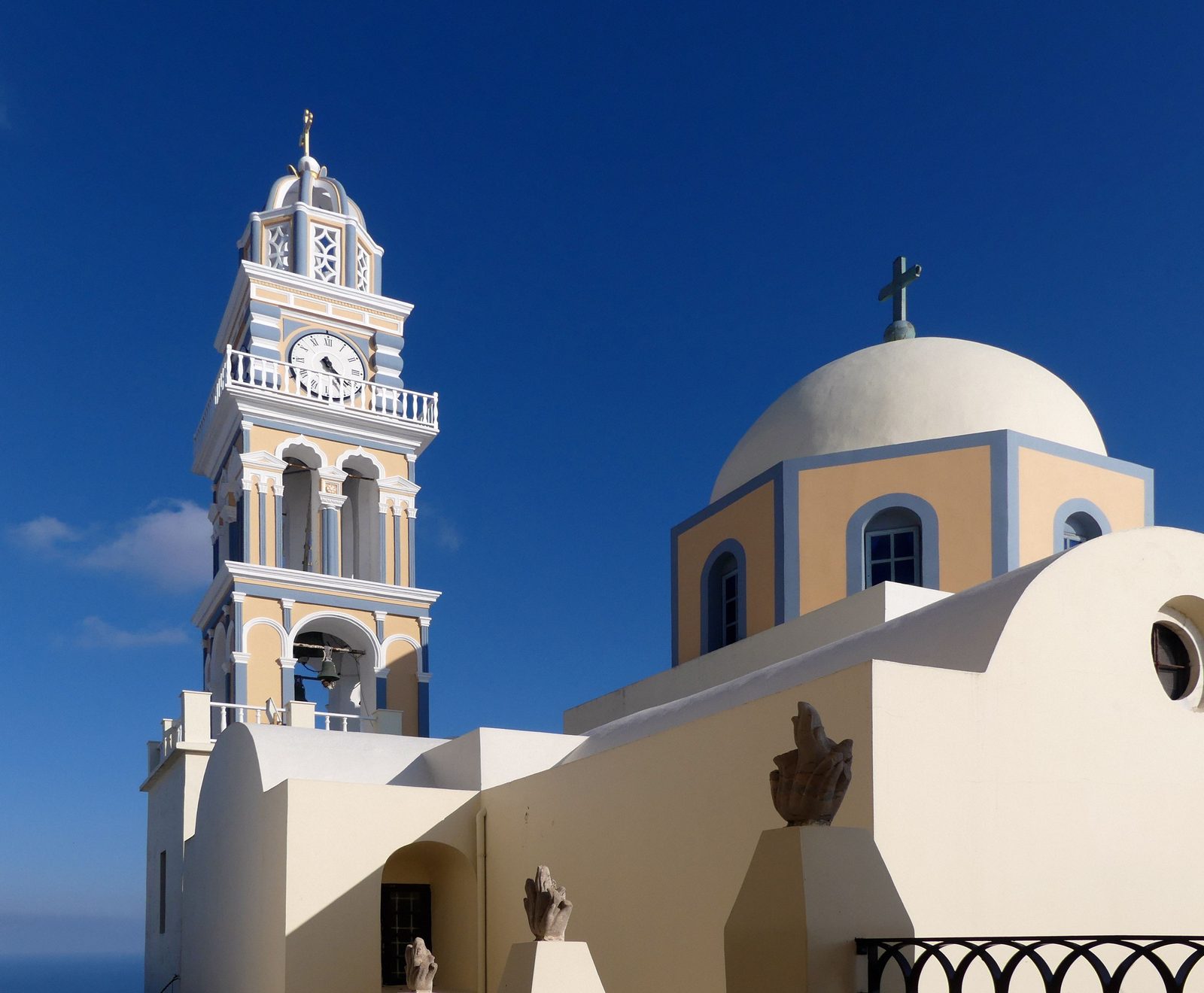 The clock tower and pale dome of the Catholic Cathedral of St John the Baptist in Fira against a blue sky