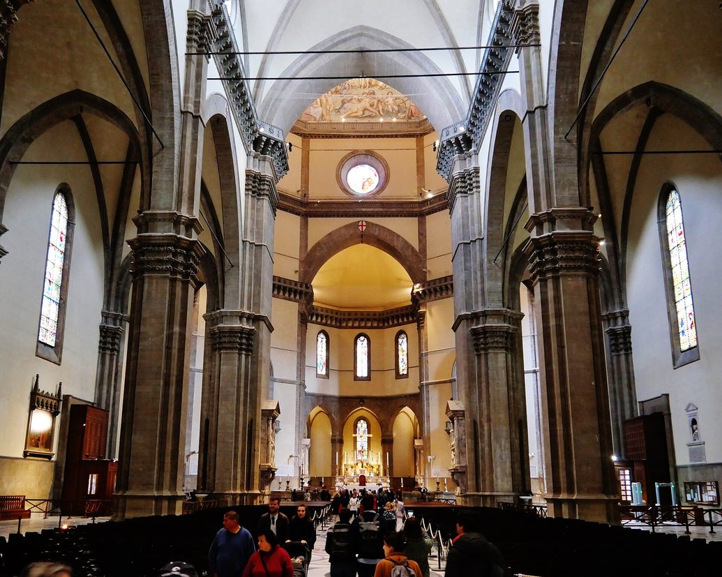 The long nave of Florence Cathedral with grey stone arches and a patterned marble floor