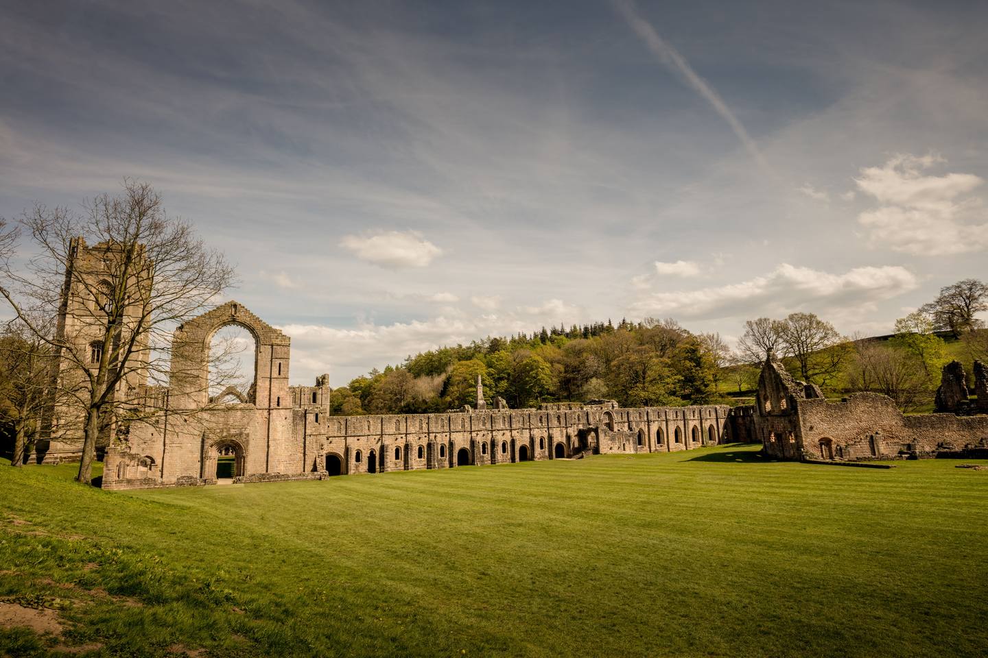 The long west range of Fountains Abbey stretching across the lawn with the tower behind