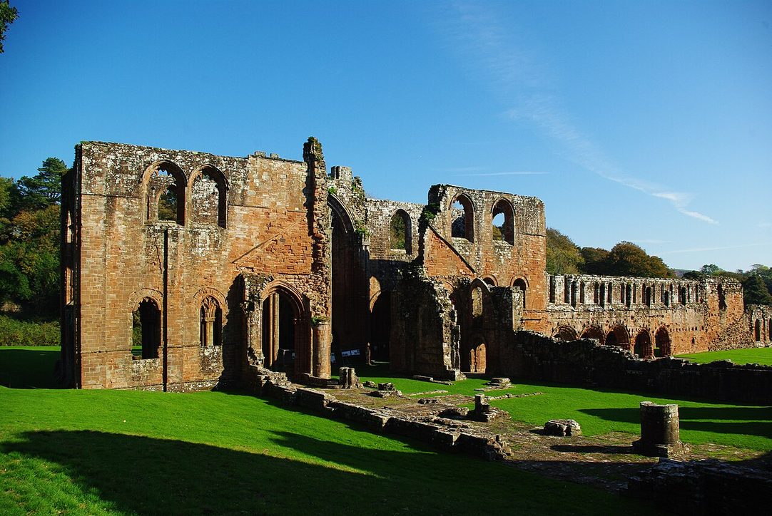 The red sandstone ruins of Furness Abbey, Cumbria, with the tall arches of the transepts and presbytery standing on a lawn